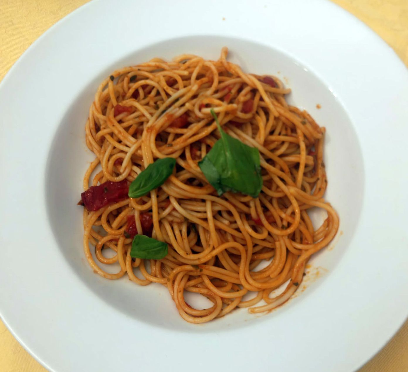 Piatto di spaghetti al sugo di pomodoro e foglie di basilico su un piatto bianco