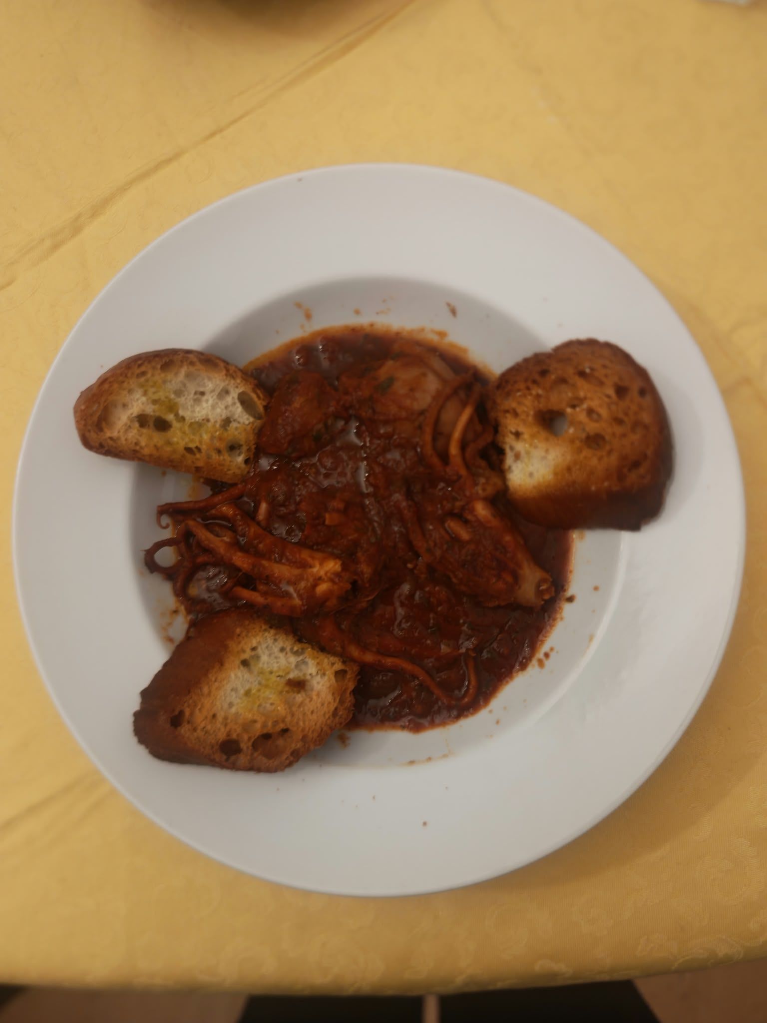 Piatto di pasta al sugo rosso con tre fette di pane all’aglio su una tovaglia gialla