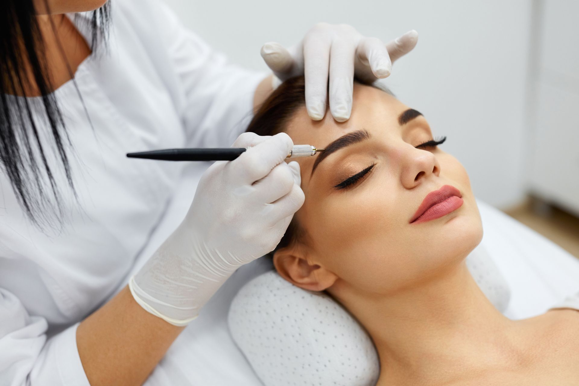A woman is getting her eyebrows tattooed in a beauty salon.