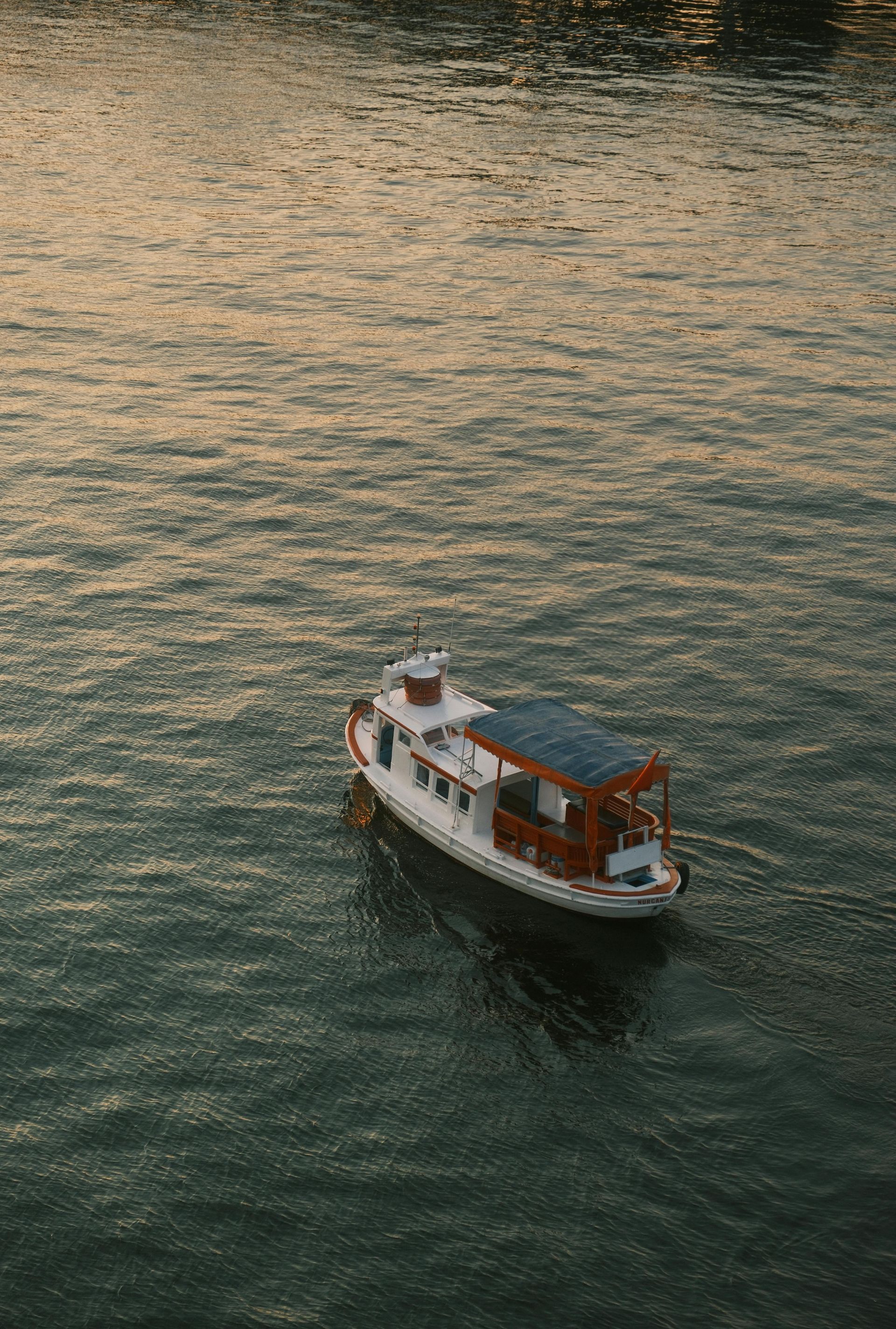 A small white and brown boat floats on shimmering water, possibly a river, with an overcast sky reflecting.