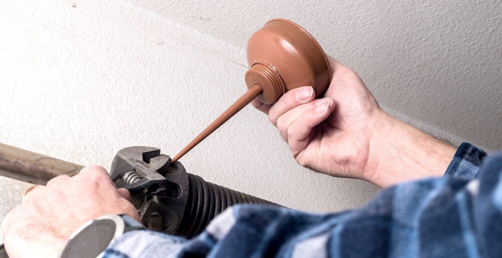 Person Lubricating a Garage Door Spring With Oil — Duncan's Doors In Highfields, QLD