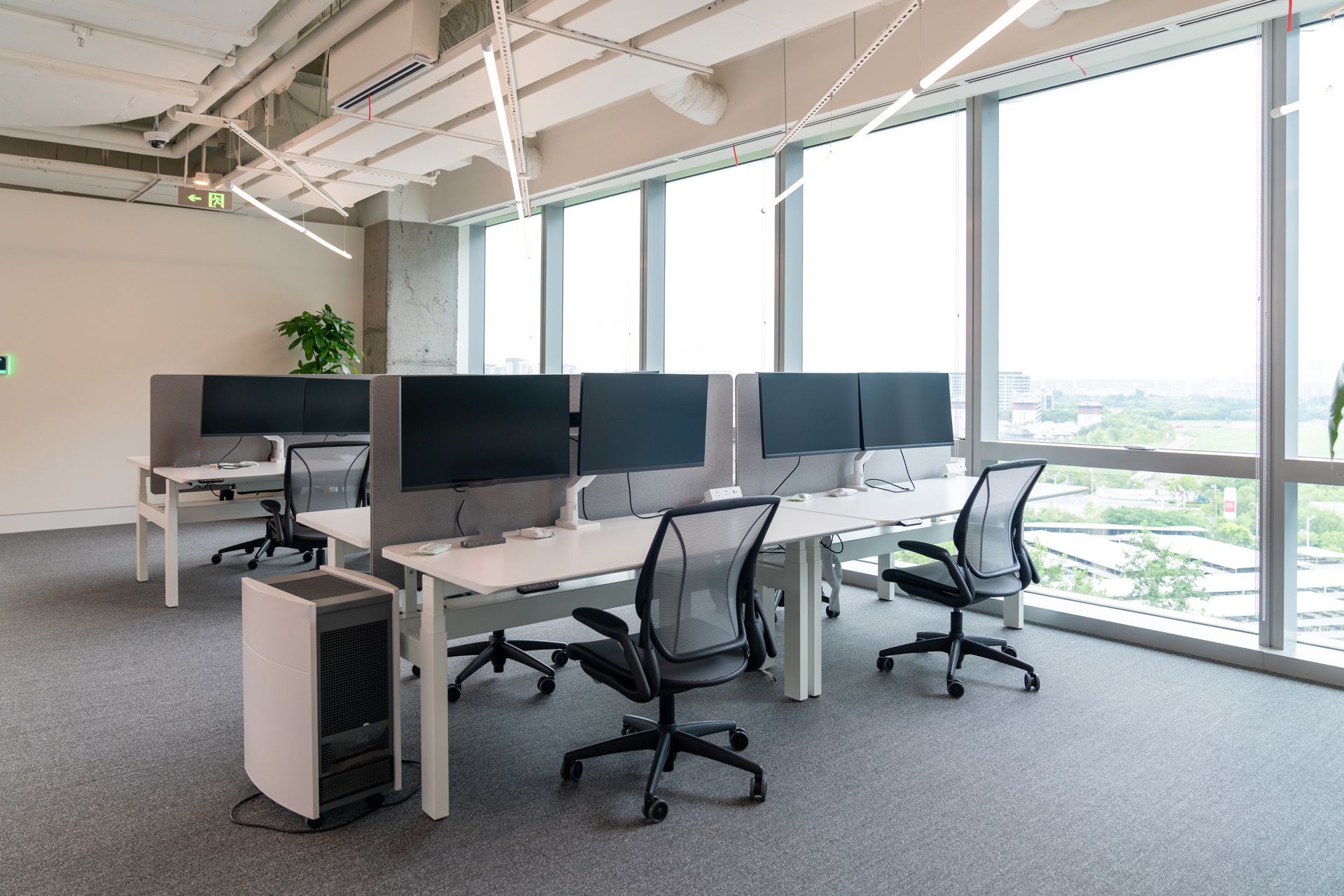 Modern office space with desks, chairs, computer monitors, and large windows.