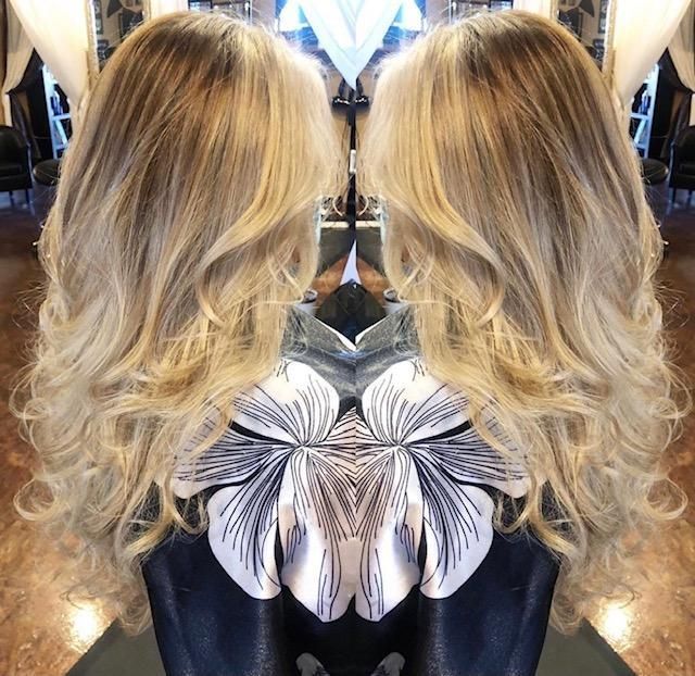 Mirrored view of a blonde wavy hairstyle with a black-and-white floral back detail on a dark top