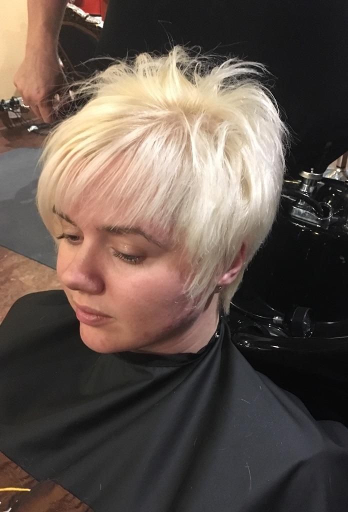 Short platinum-blonde haircut on a person in a salon chair, wearing a black cape.
