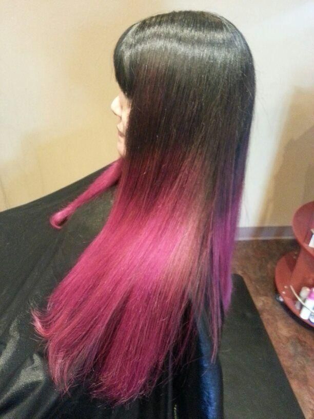 Long straight hair with black roots fading to bright pink, shown from the side in a salon chair