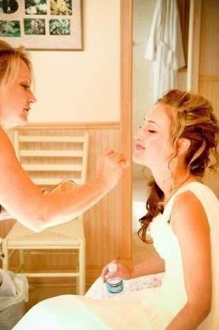 Woman applying makeup to seated woman in a bright bedroom