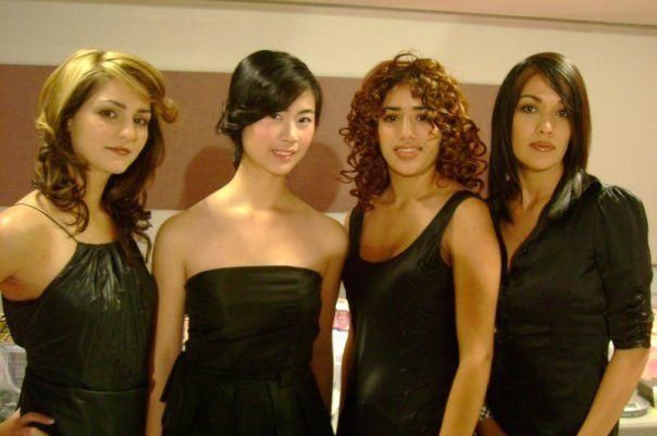 Four people posing together in black dresses against a warm indoor background