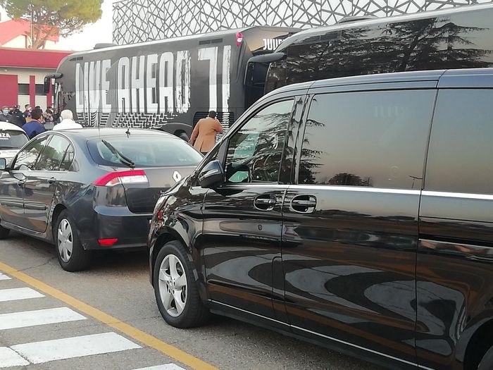 Auto in transito accanto a un muro nero con grandi scritte bianche in corrispondenza di un attraversamento pedonale.