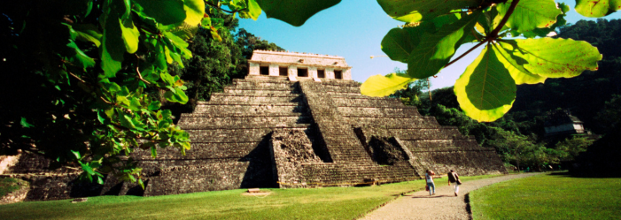 Antigua pirámide maya rodeada de vegetación y cielo.