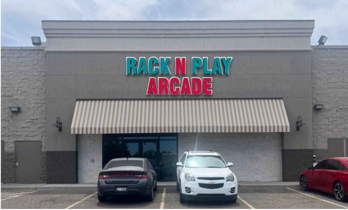 Storefront of “Back N Play Arcade” with striped awning and parked cars in front