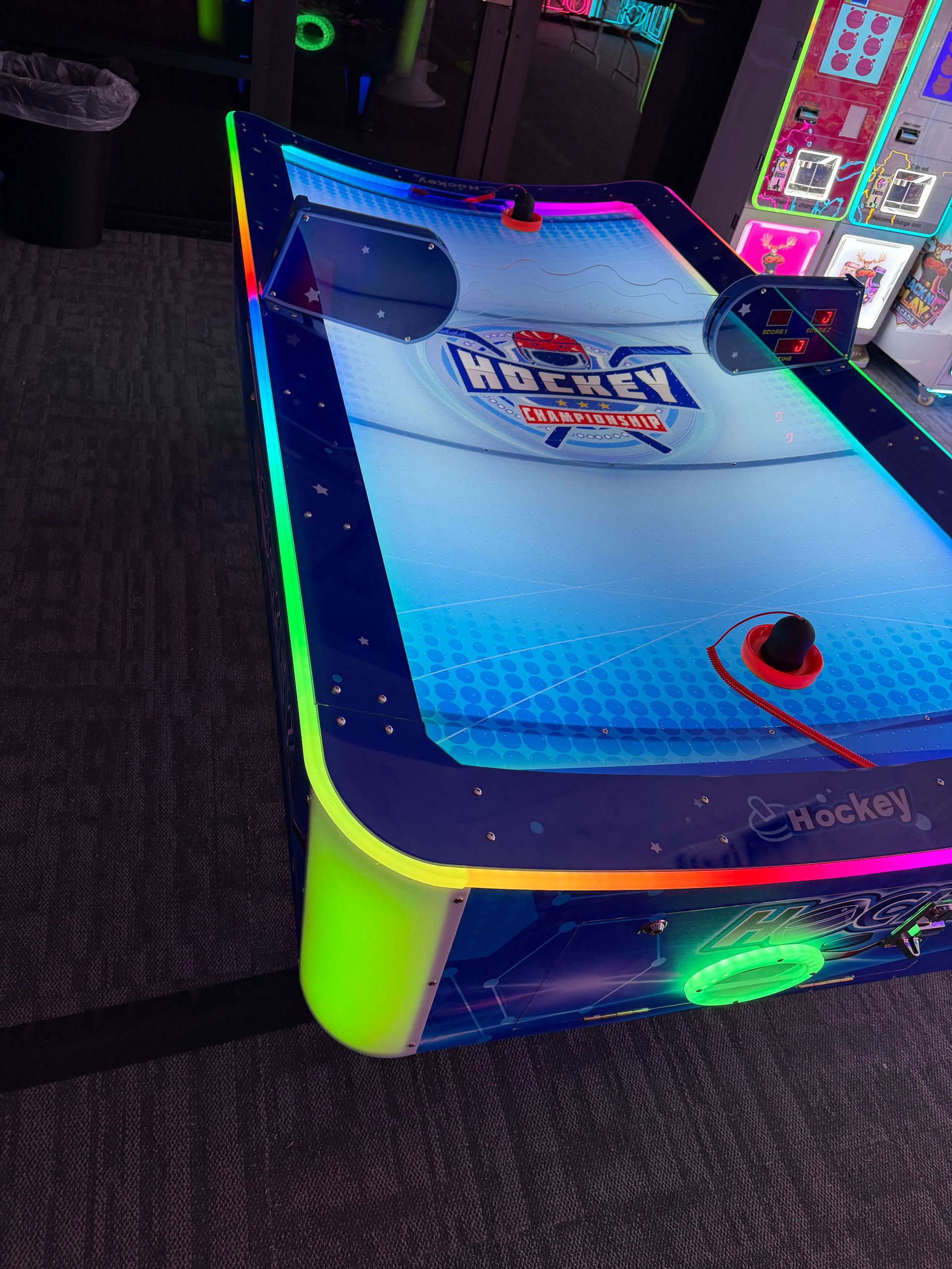Neon-lit arcade air hockey table with blue playing surface and glowing green accents.