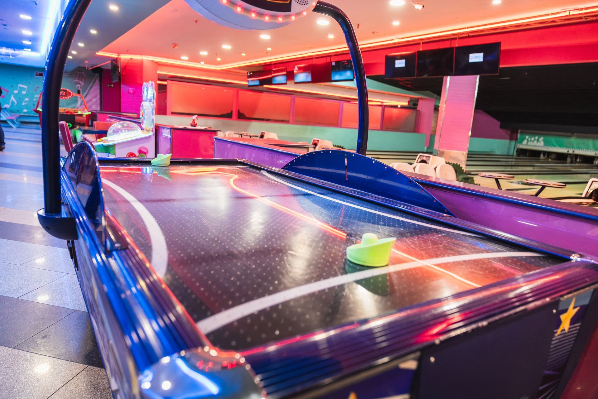 Colorful neon-lit air hockey table in an arcade, with glowing rails and a puck near the center.