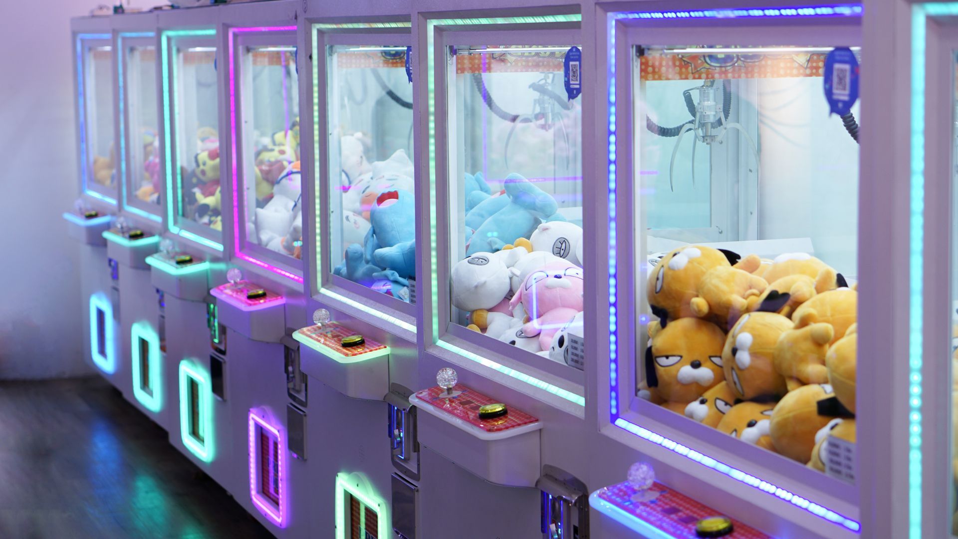 Row of glowing claw machines with plush toys in a colorful arcade