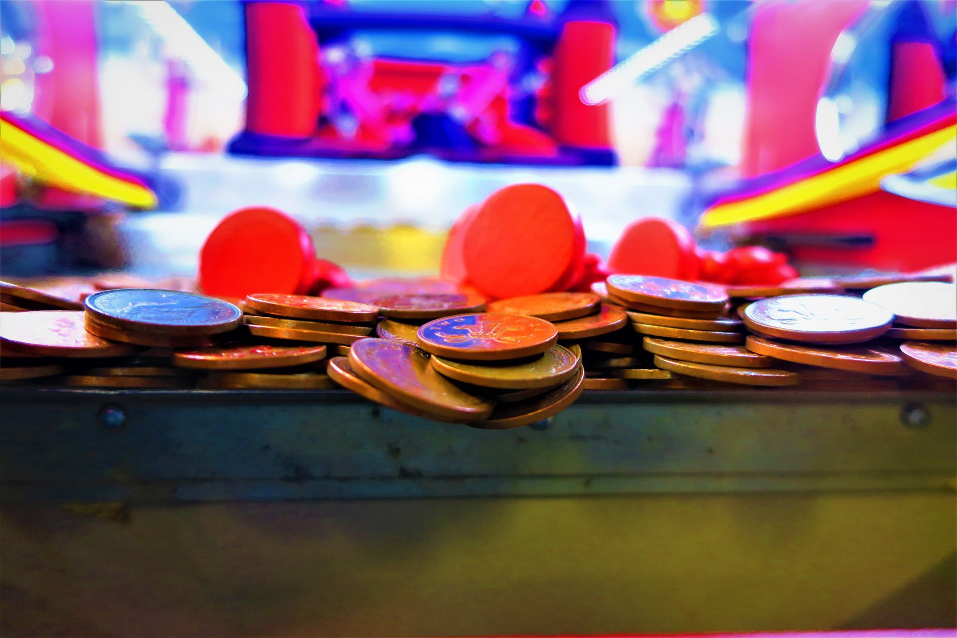 Stack of coins and red tokens on a brightly lit arcade or casino game table.