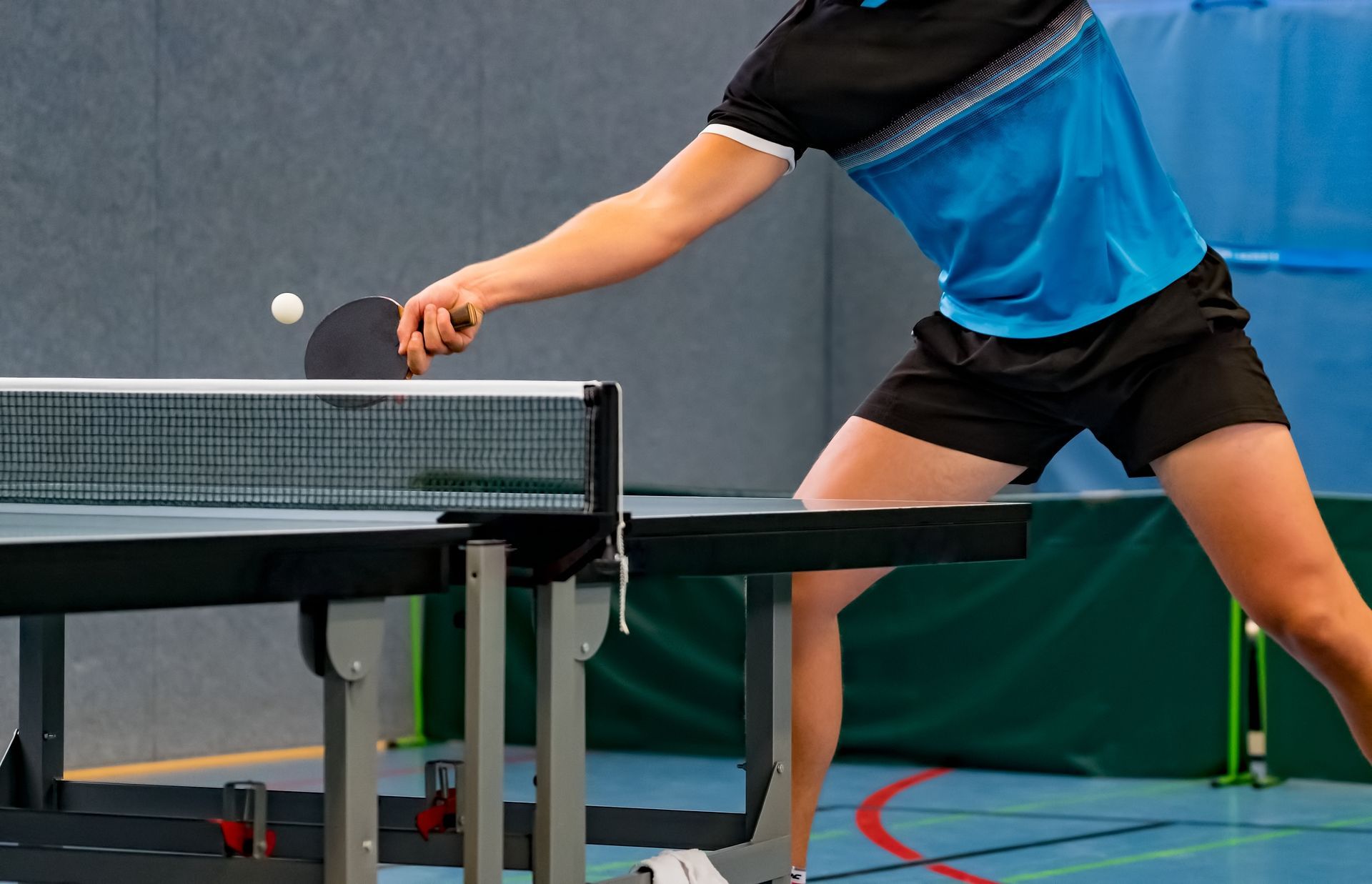 Ping-pong player reaching for a shot at the table in a gym