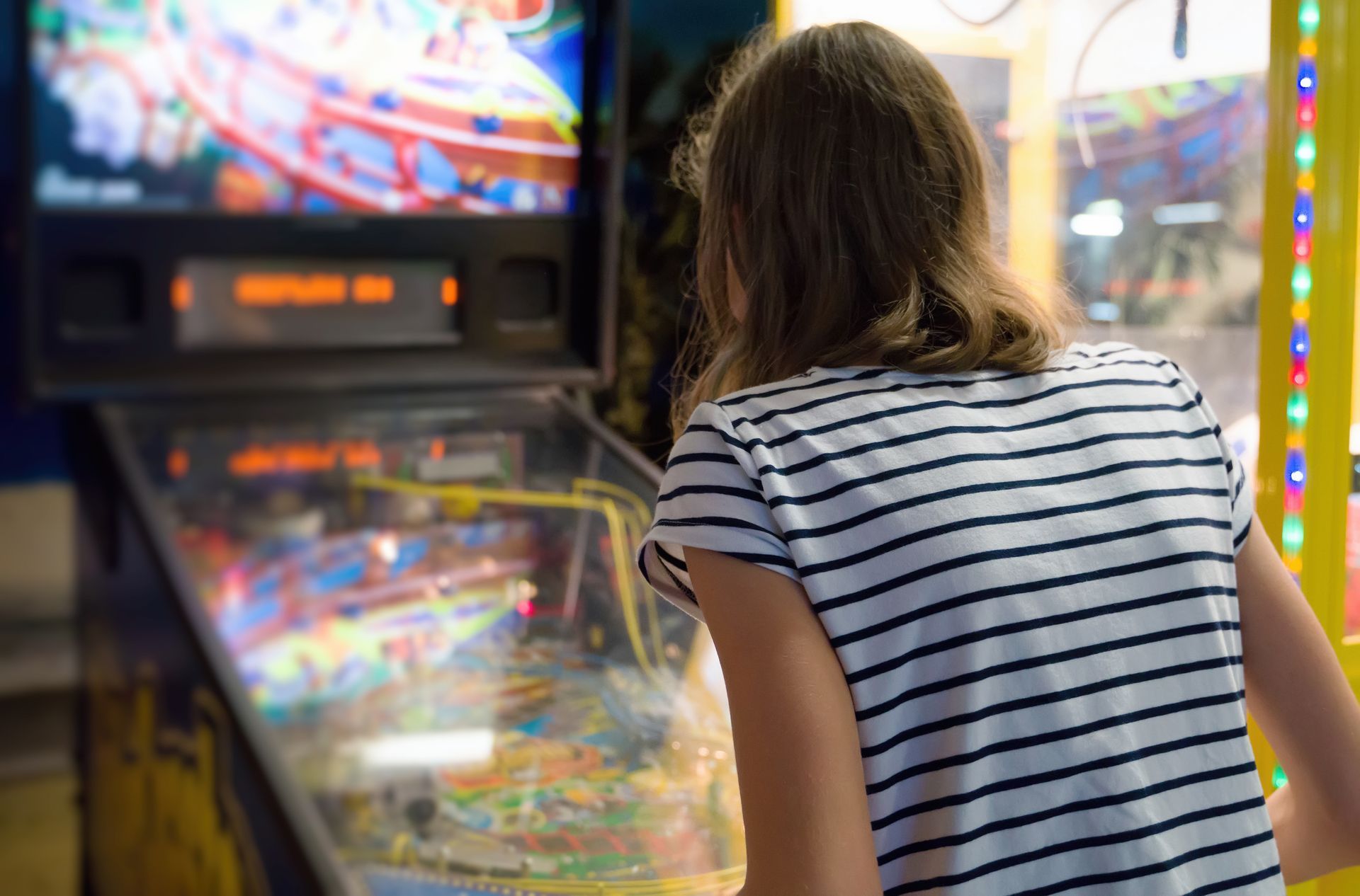 Person in a striped shirt playing a pinball machine in an arcade