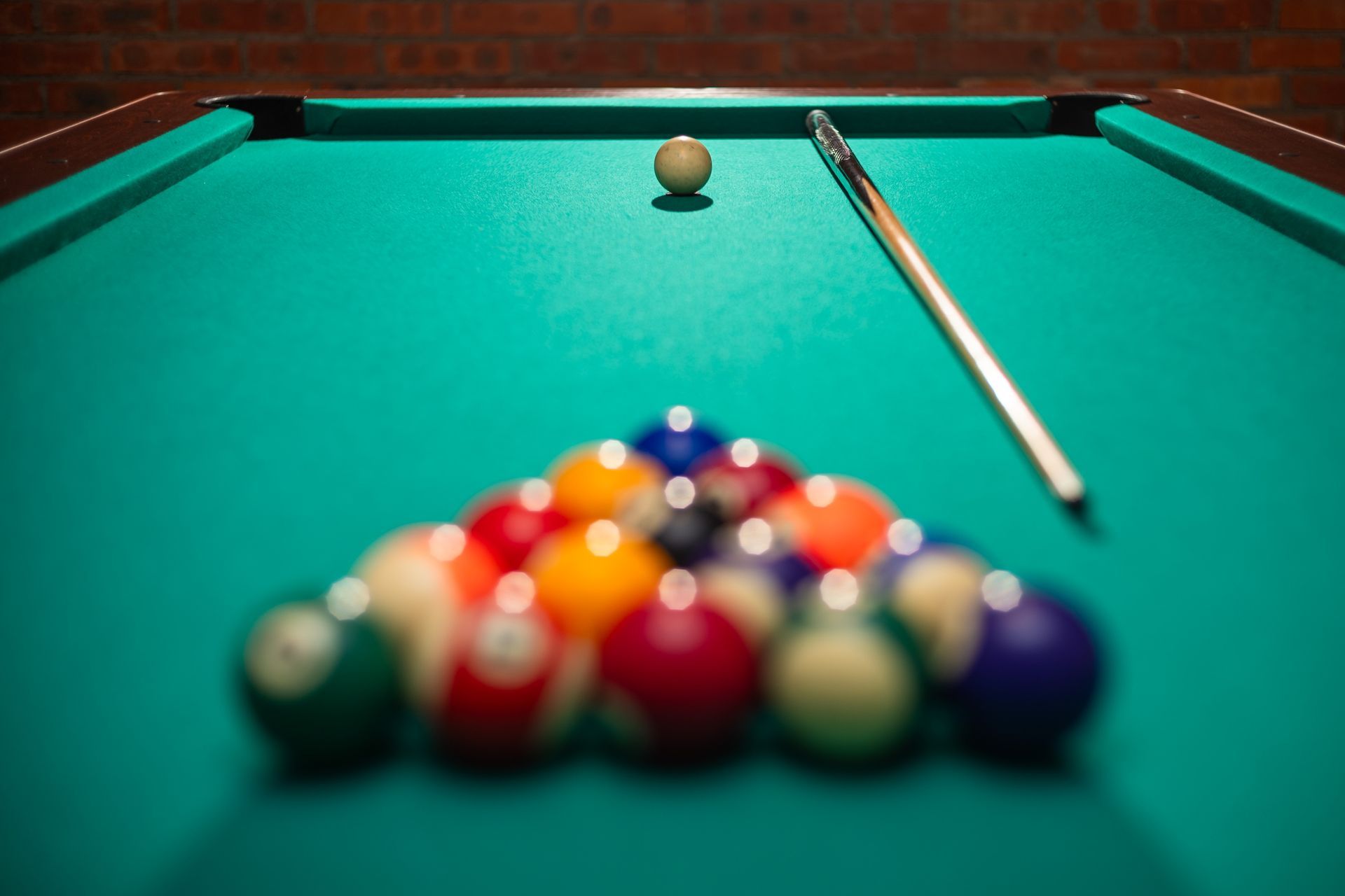 A pool table with racked balls, a cue stick, and the cue ball ready for a break shot.