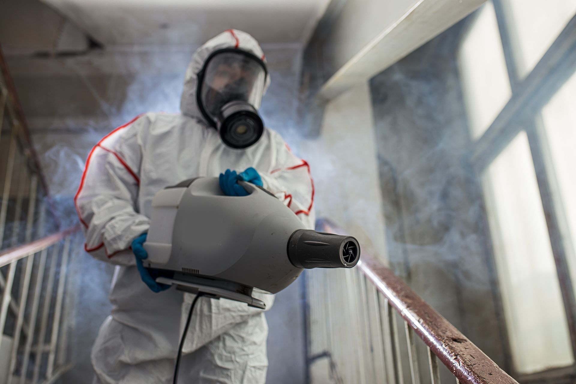 A man in a protective suit is disinfecting a building with a machine.