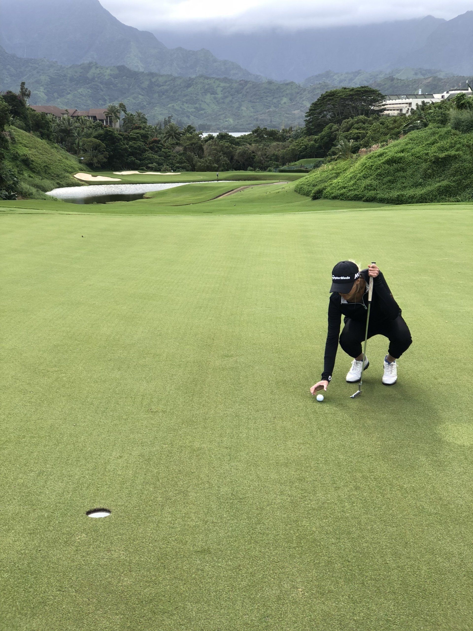 A person lines up a golf putt on a green, with a mountain range in the background.