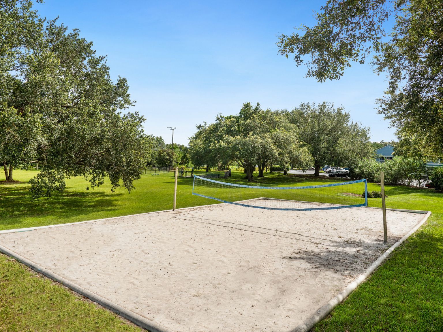 Sand volleyball court surrounded by green grass and trees under a blue sky. Schedule a tour to experience the relaxed lifestyle offered by these Melbourne, FL apartments.