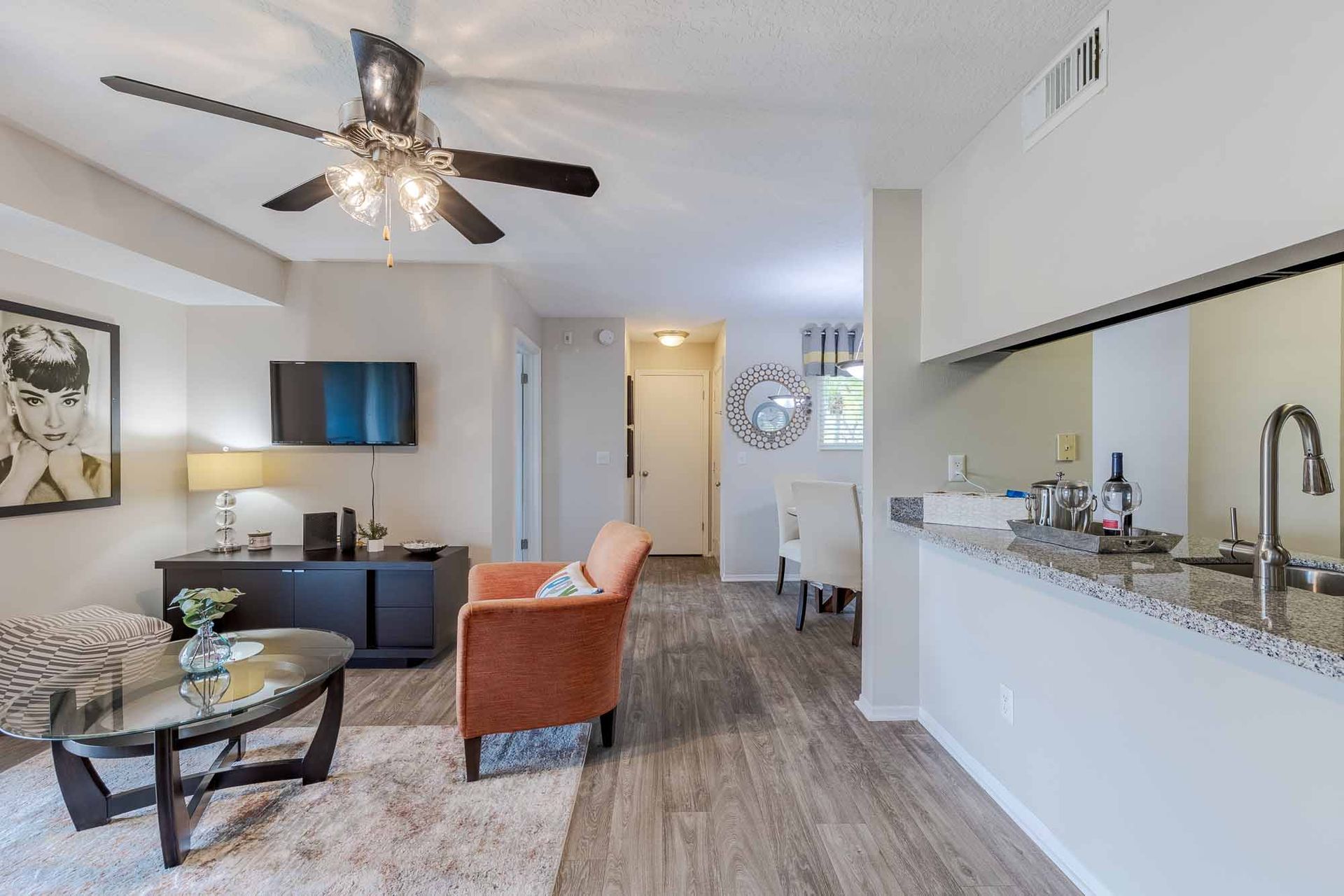 Living room with TV, orange armchair, and open kitchen with granite countertop.