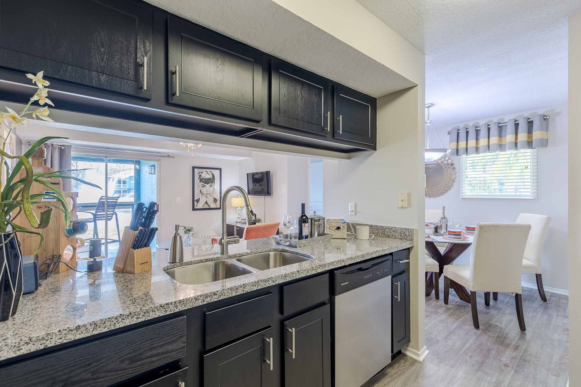 Kitchen with black cabinets, granite countertops, and stainless steel appliances. Dining area visible. Discover modern living at Savannahs at James Landing—tour these stunning Apts for rent in Melbourne, FL today.