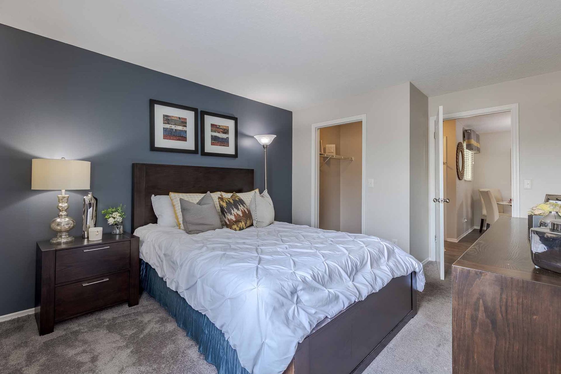 Bedroom with a navy accent wall, bed with white comforter, two framed pictures, and a lamp on the nightstand. Bring your furry companion and explore our Pet-friendly aparmtents in Melbourne, FL with a personalized tour.