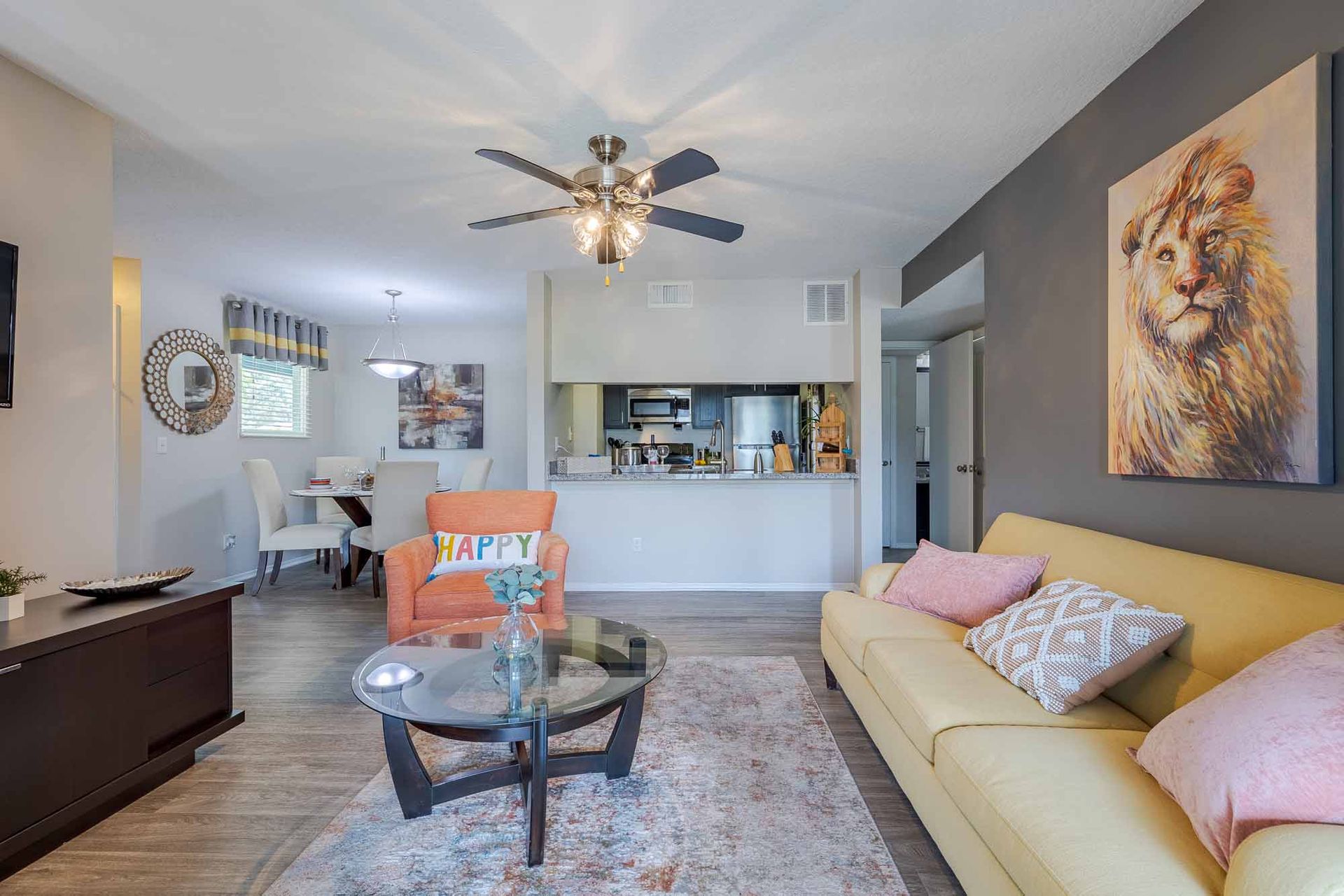 Living room with yellow couch, orange chair, and open view of dining area. Explore our spacious 2-bedroom apartments in Melbourne, FL—schedule a tour and picture life here.