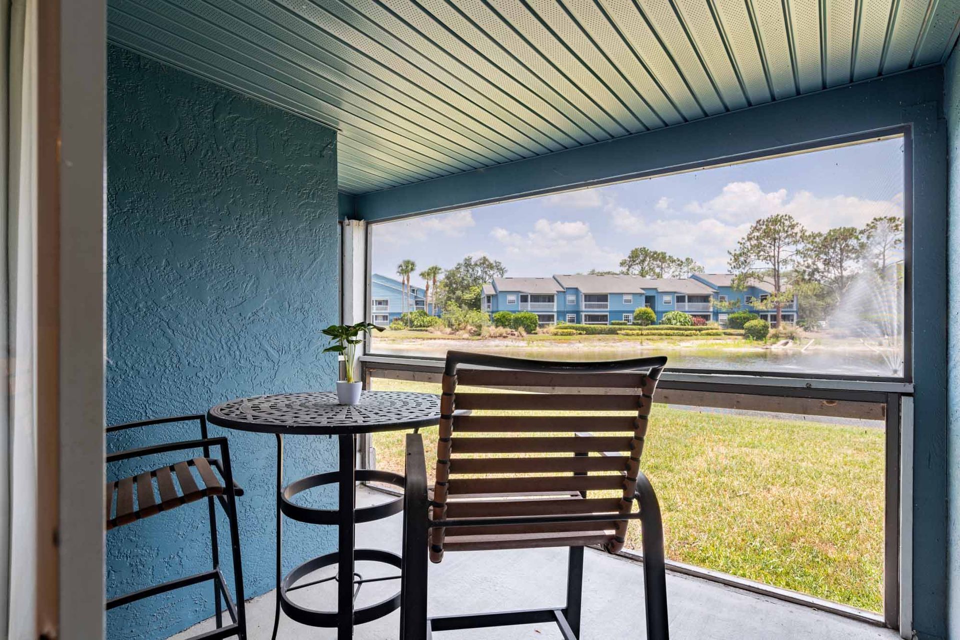 Balcony with a table and chairs overlooking a pond and distant buildings. Blue walls and ceiling. See yourself at home in our stylish 1-bedroom apartments in Melbourne, FL by booking a tour.