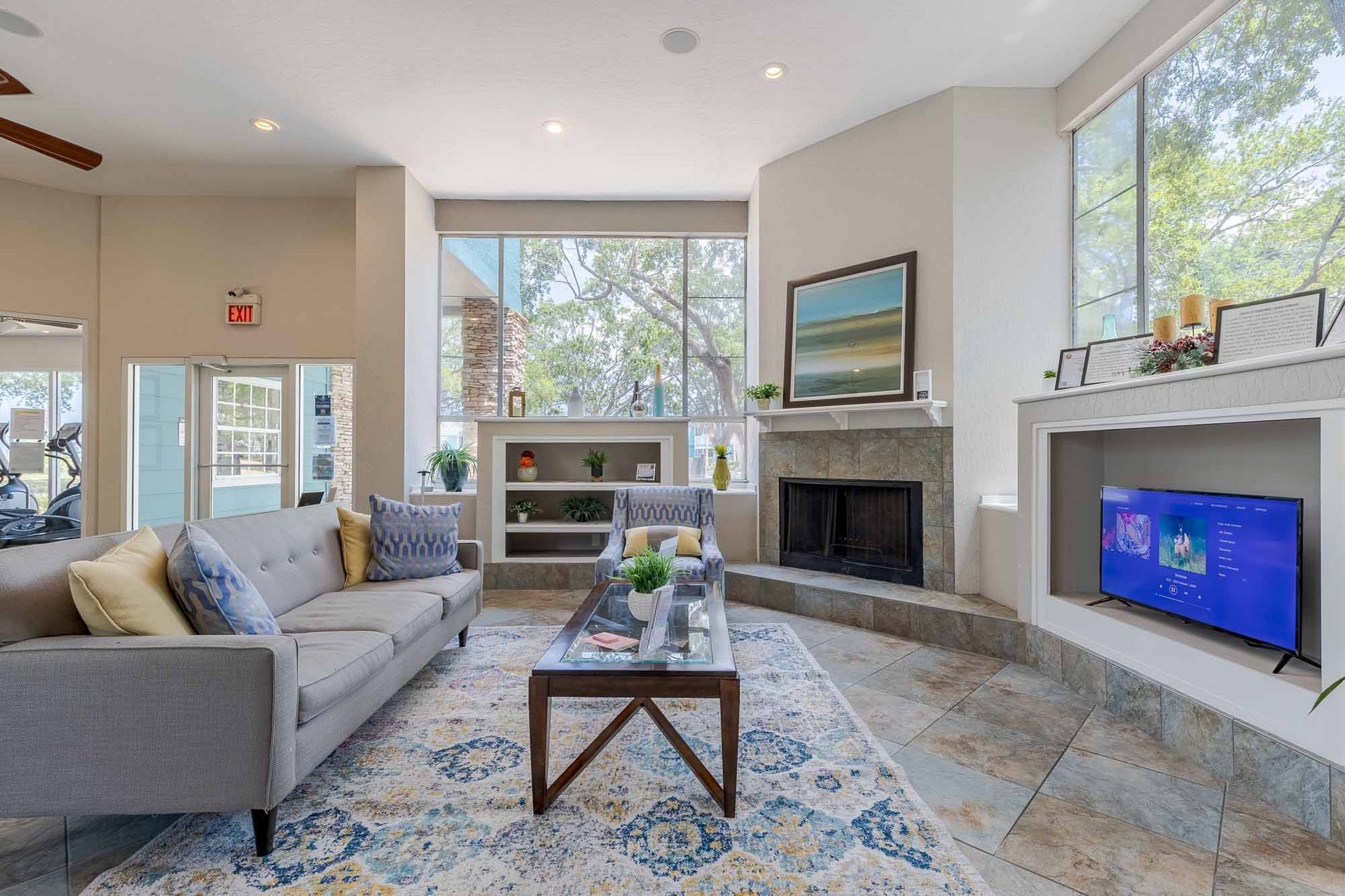Resident clubhouse lounge area with gray sofa, fireplace, large windows, and a rug. Explore the comfort and space of our 2-bedroom apartments in Melbourne, FL during your private tour.