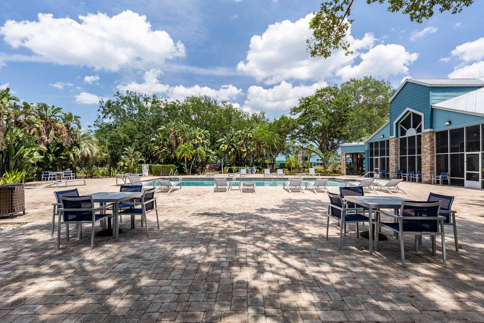 Outdoor patio with tables, chairs, and a swimming pool in a sunny setting. Take a tour of our cozy 1-bedroom apartments in Melbourne, FL and envision your new space.