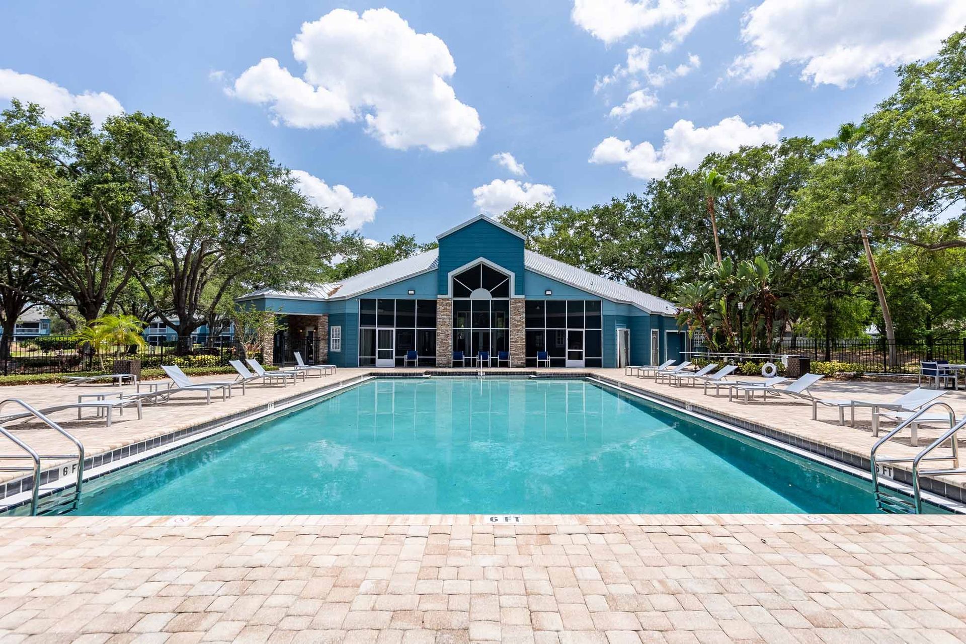 Swimming pool in front of a blue building with white roof, trees, and sky. Lounge chairs surround the pool. See why renters love these Apts for rent in Melbourne, FL by visiting Savannahs at James Landing.