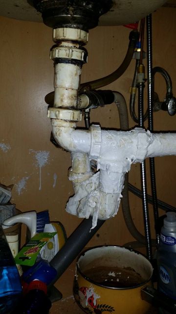 A sink with a lot of pipes underneath it and a bowl of water.