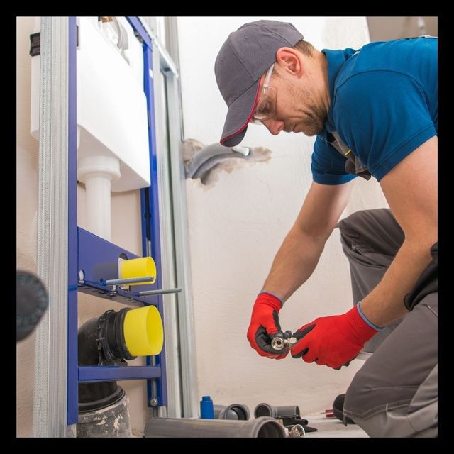 A plumber is working on a toilet in a bathroom.
