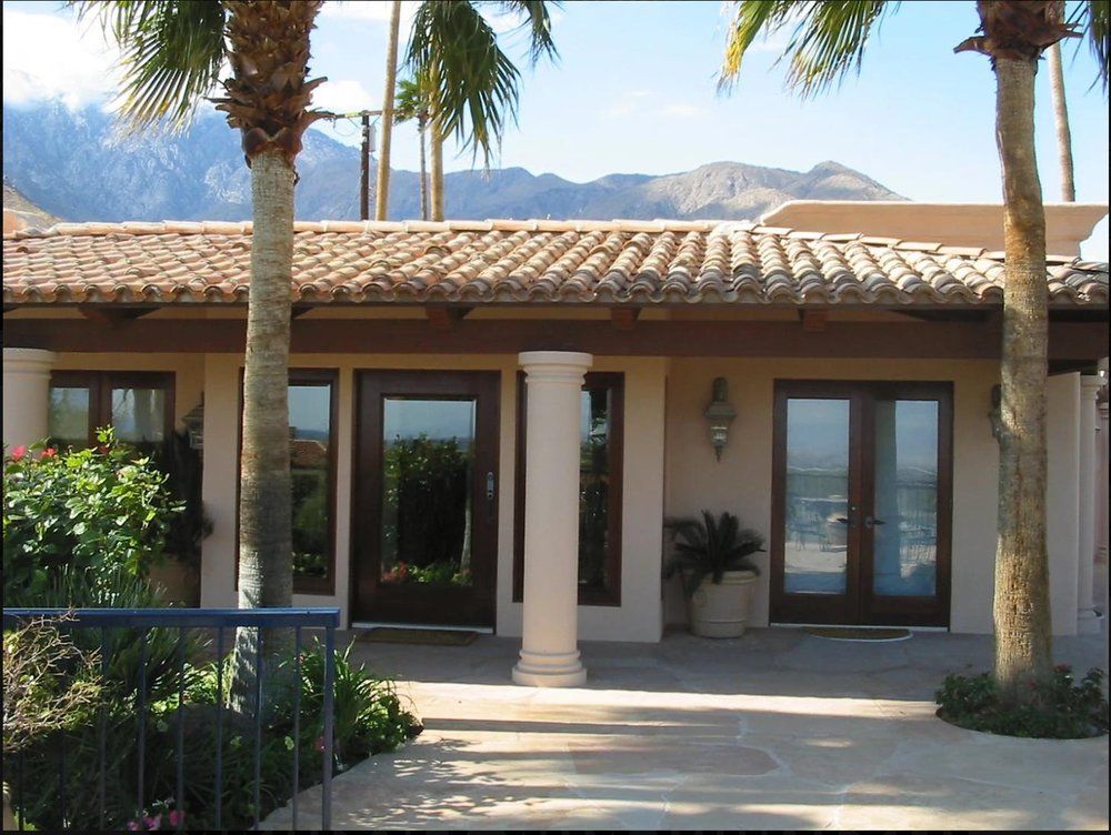 Spanish-style house entrance with columns, palm trees, and mountains in the background