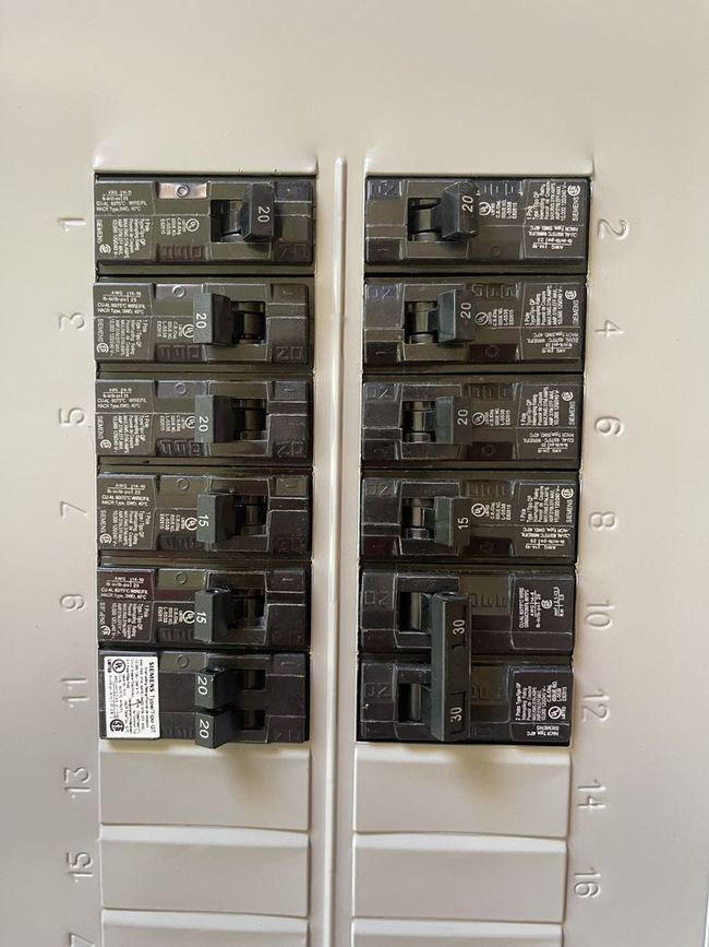 Two rows of electrical circuit breakers on a white panelboard.