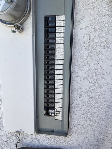 Electrical breaker panel in a wall, with labeled switches and a round meter nearby.
