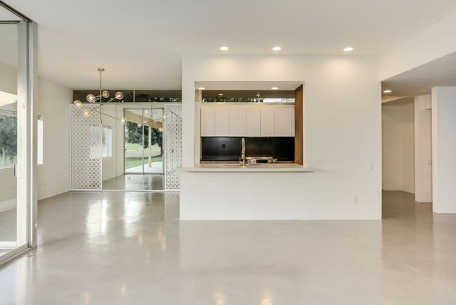 Bright empty modern living room with polished floors, kitchen pass-through, and large windows with a glass door