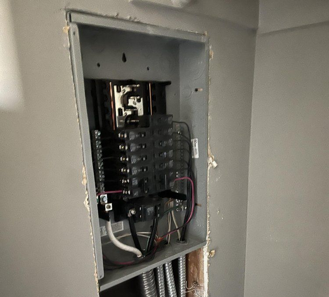 Open electrical breaker panel with exposed wiring in a wall cavity