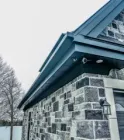 A dark-colored, stone-walled building exterior featuring an outdoor security camera mounted under the roof eaves.