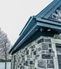 A dark-colored, stone-walled building exterior featuring an outdoor security camera mounted under the roof eaves.