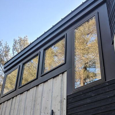Modern home exterior featuring large windows, dark metal siding, and vertical light-toned wood cladding.
