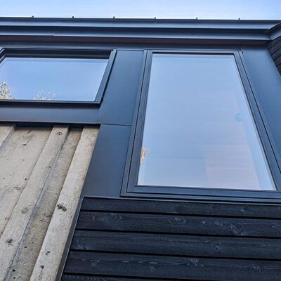 An exterior view showing horizontal black wood siding beside vertical light-colored panels and two modern glass windows.