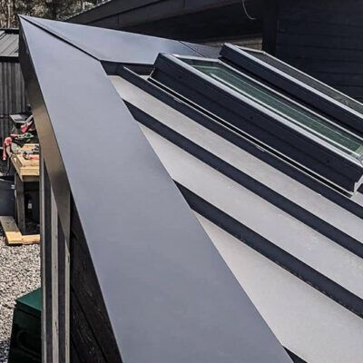 Close-up of a modern, angled dark metal roof edge featuring a series of integrated glass skylights.