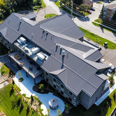 An aerial view of a multi-story building with a gray metal roof, featuring a rear deck and a gazebo on a paved patio.