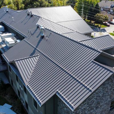 An aerial view of a building with a dark grey, standing-seam metal roof with several ventilation units and gables.