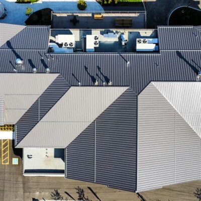 Aerial view of a commercial building with a metal roof, showing rooftop HVAC units and a parking area.
