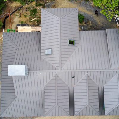An aerial view of a gray metal roof with multiple gables, ridges, skylights, and a chimney.