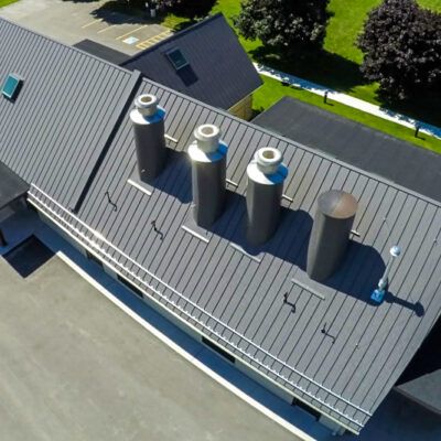 Aerial view of a gray metal roof featuring four industrial chimneys, a snow guard rail, and a skylight.