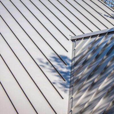A close-up view of a metal roof with diagonal raised seams and a corner section featuring light and shadow patterns.
